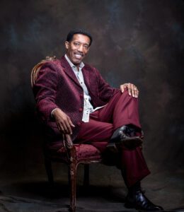 A person posing for a photograph while wearing a maroon suit
