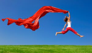 A woman jumping up in the air while holding a piece of red cloth