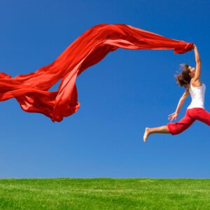 A woman jumping up in the air while holding a piece of red cloth